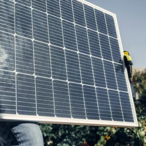 Close-up of technician with safety gear installing a solar panel outdoors.