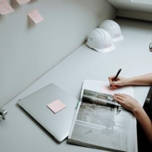 Professional architect making notes in a modern office with a laptop and safety helmets.